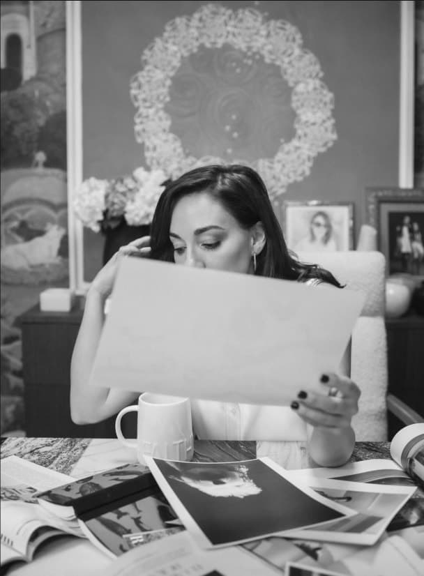 Cordelia, en blanco y negro, sentada a una mesa revisando pruebas impresas.